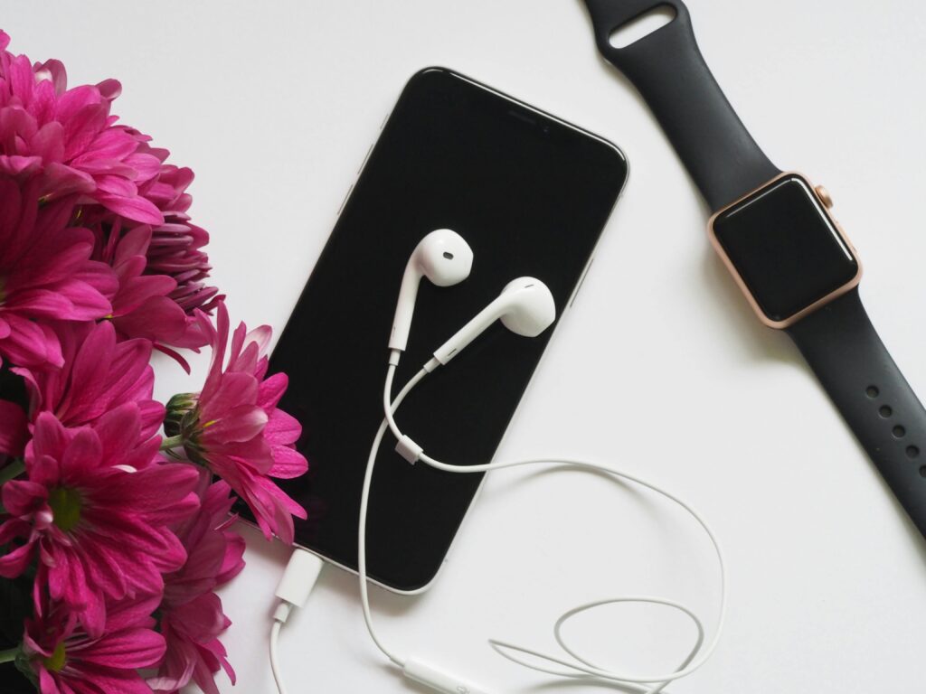 pexels-photo-748598-748598 A flat lay of smartphone, smartwatch, and earphones beside vibrant pink flowers on a white background.