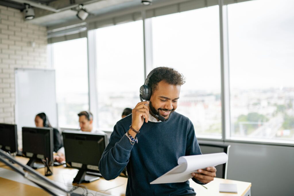 pexels-photo-8867250-8867250 Friendly call center agent engaged in conversation while reviewing documents at his desk.
